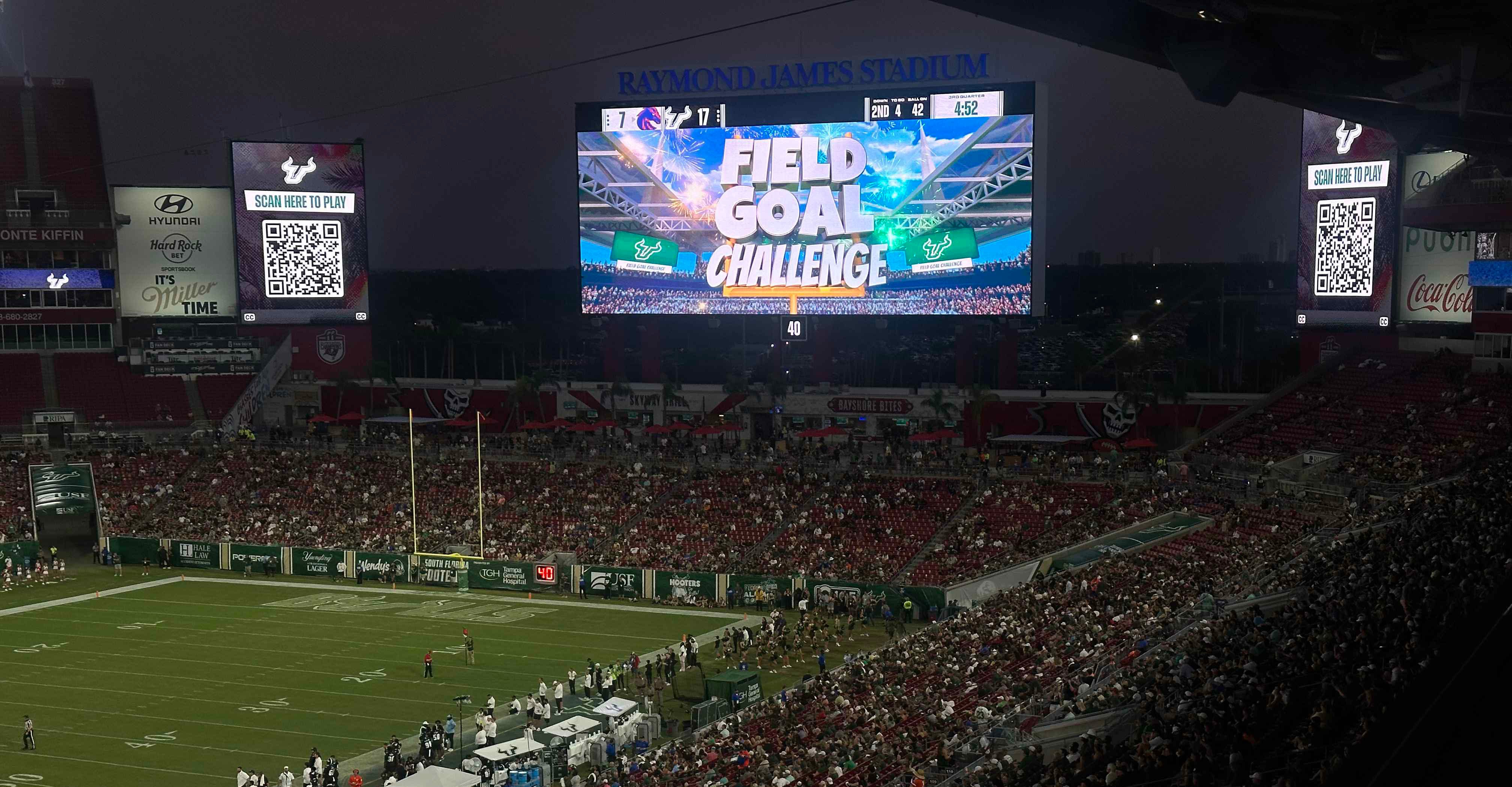 Packed football stadium at night featuring a large video board displaying a venue4D interactive Field Goal Challenge game, with QR codes for real-time fan participation.