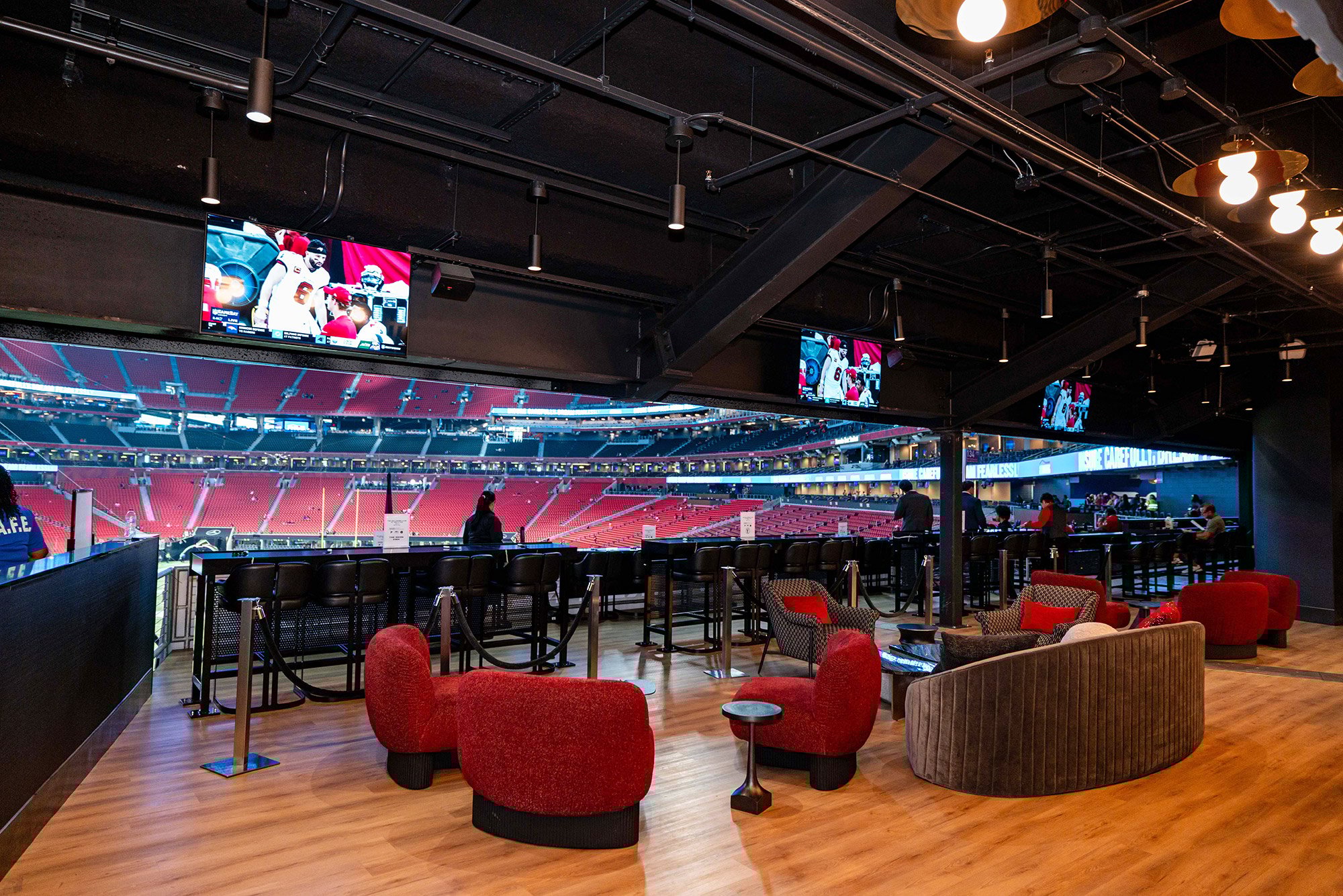 An empty corporate suite overlooking a football game, with vacant premium seats and the field visible below.
